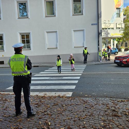 Zwei Volkschulkinder überqueren unter der Aufsicht einer Polizistin die Straße 