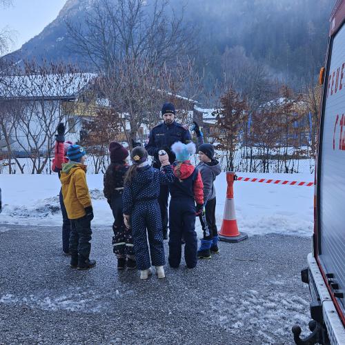 Der Polizist und die Schüler stehen hinter dem Feuerwehrauto 