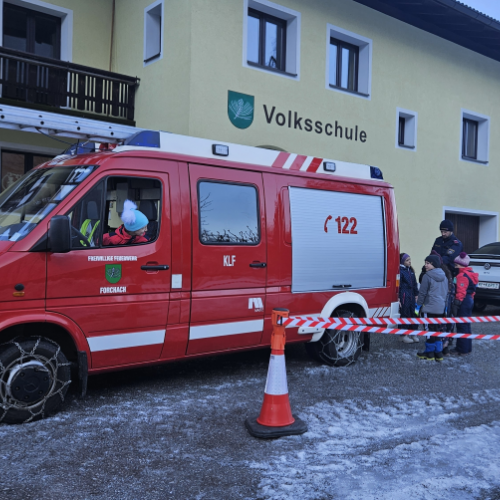 Eine Schülerin sitzt im Feuerwehrauto und mehrere Kinder stehen hinter und neben dem Feuerwehrauto.