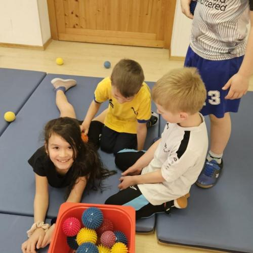 Zwei Schüler massieren mit Bällen eine Schülerin 