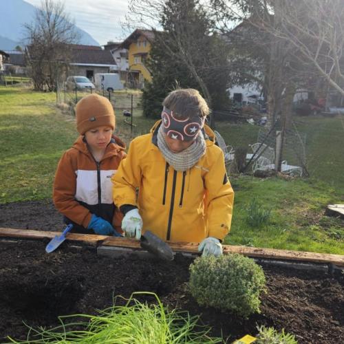 Drei Schüler stehen mit Gartenschaufeln hinter dem Hochbeet
