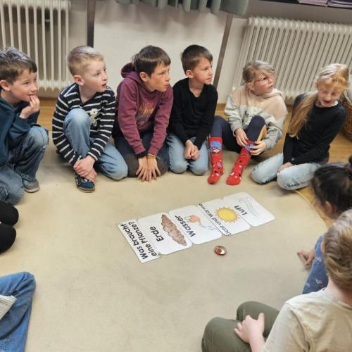 Schüler sitzen im Sitzkreis , Anna erklärt ihnen was die Kresse zum Wachsen benötigt 