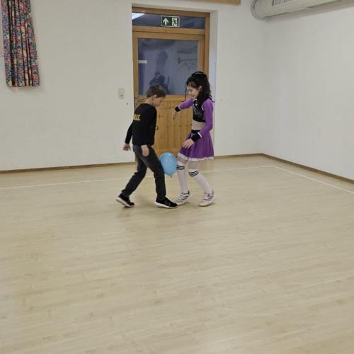 Zwei Kinder tanzen mit einem Luftballon zwischen den Knien 