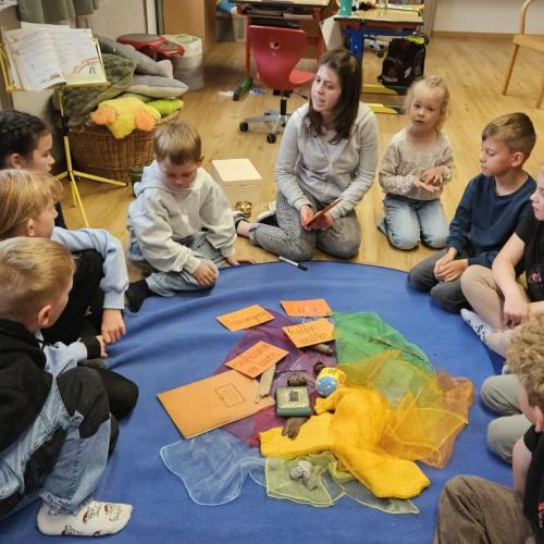 Die Praktikantin bespricht mit den Schülern ihr Prjekt, in der Mitte liegen verschiedene Dinge aus der Vergangenheit 