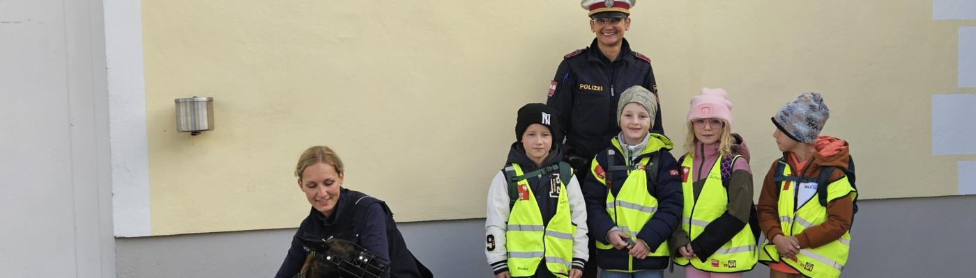 Volkschulkinder mit zwei Poluistinnen und dem Polizeihund vor der Polizeistelle