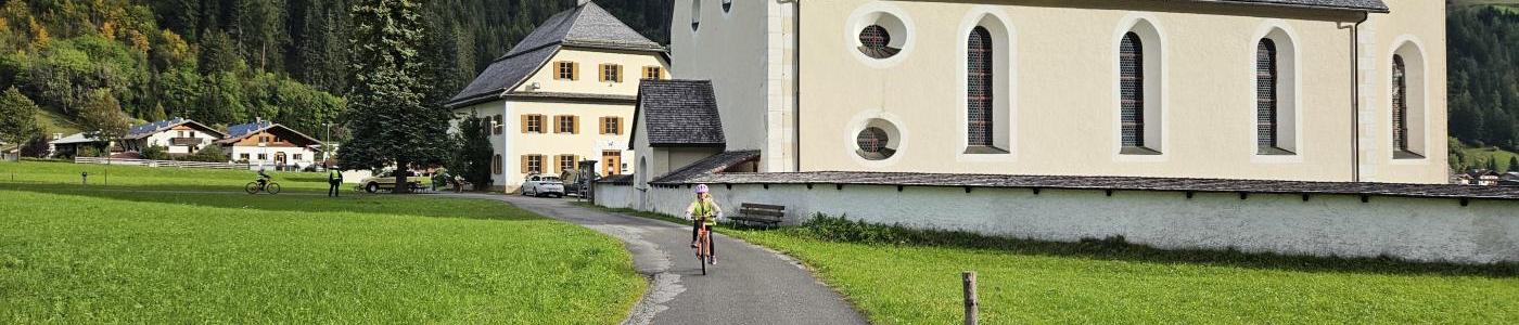 Ein Kind fährt mit dem Fahrrad im Hintergrund ist die elbigenalper Kirche 